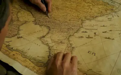 La persona de habla hispana que escribe algo en papel mientras mira un viejo mapa o documento que ilustra su historia e influencia ancestral. Esto puede incluir conquistas militares o migraciones a diferentes regiones del pasado